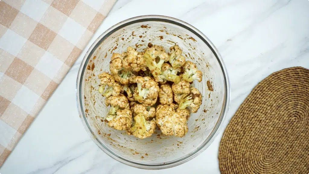 Cauliflower florets coated in a seasoning mix in a glass bowl