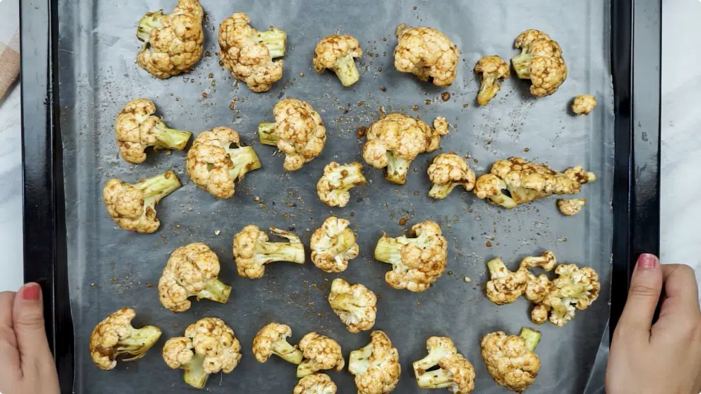 Raw cauliflower florets covered in a seasoning mix spread on a baking sheet lined with paper