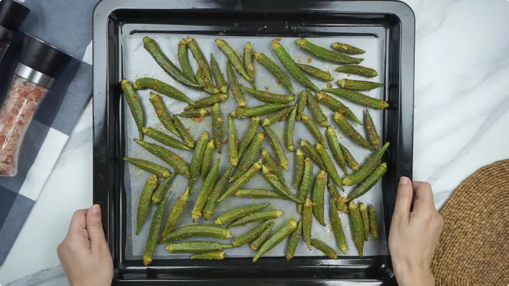 Okra spread out on a baking sheet lined with parchment paper for roasting