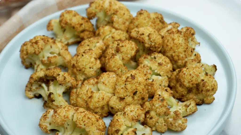 Cooked cauliflower florets roasted with lots of seasoning and spices on a white plate