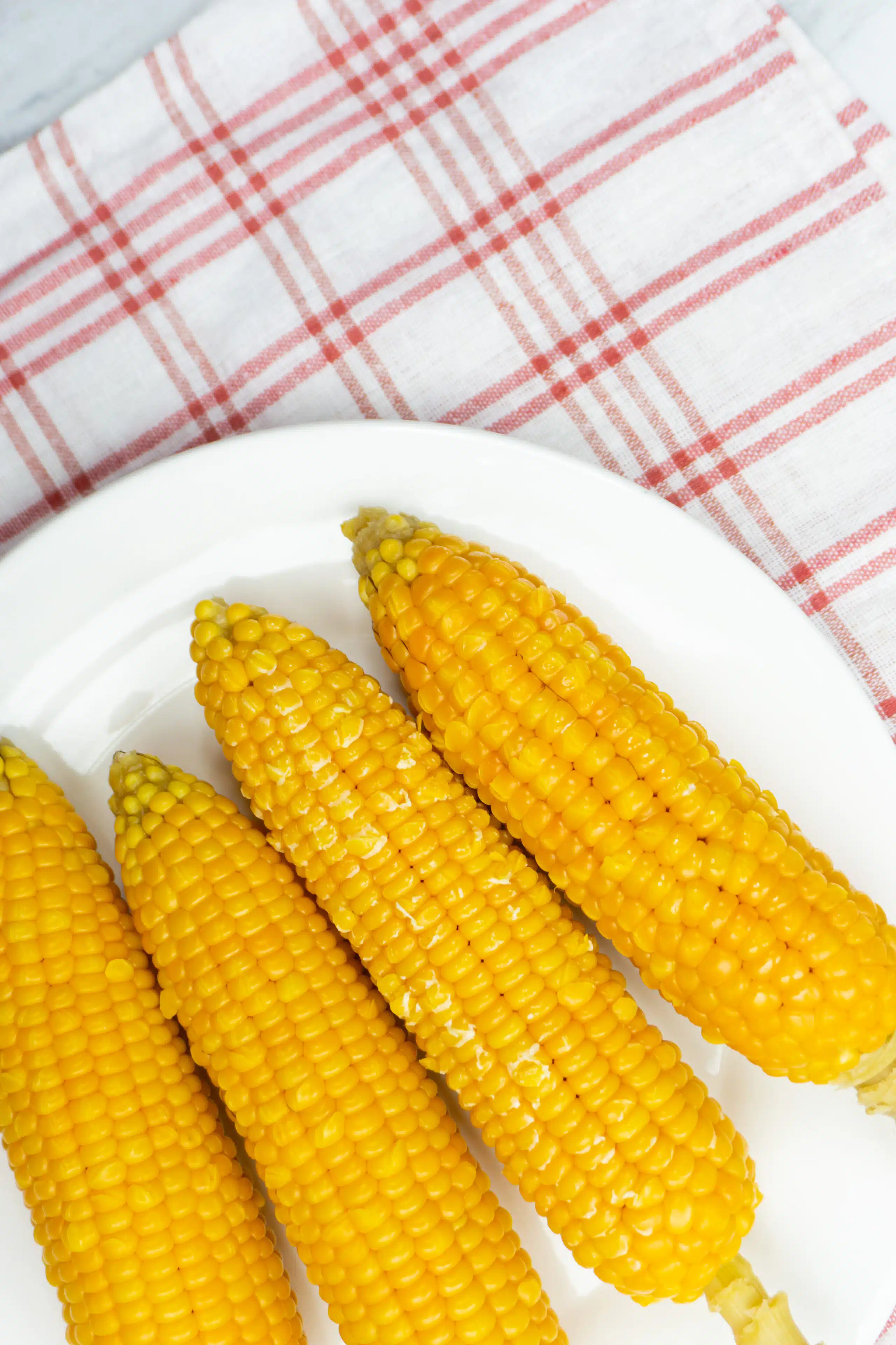 4 corn on the cob on a white plate with chequered tea towel background