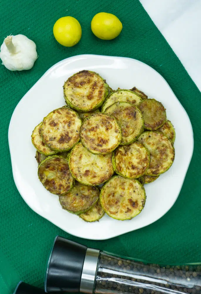 Roasted courgettes on a white plate with lemons in the background
