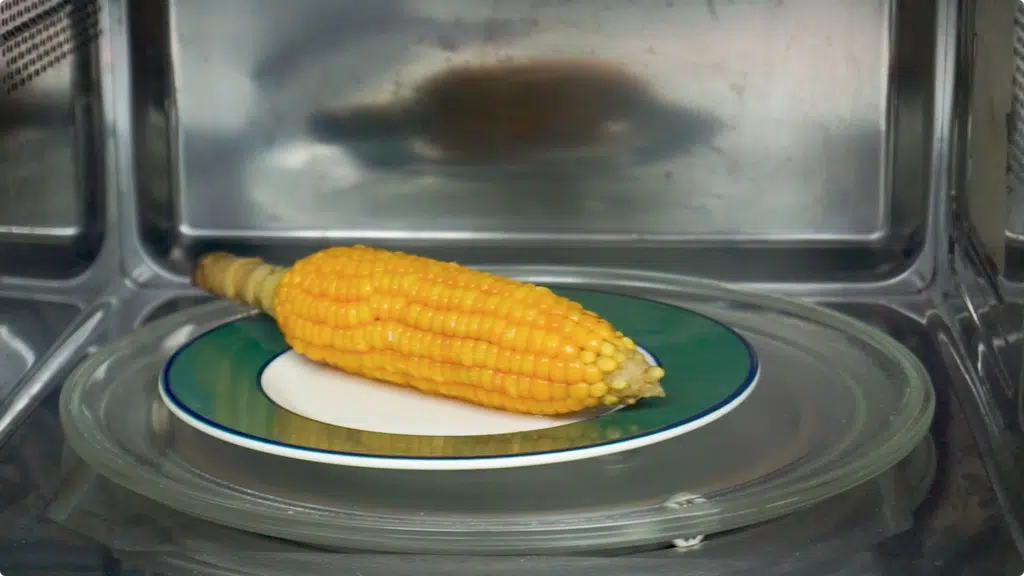 A single corn on the cob being reheated in a microwave oven