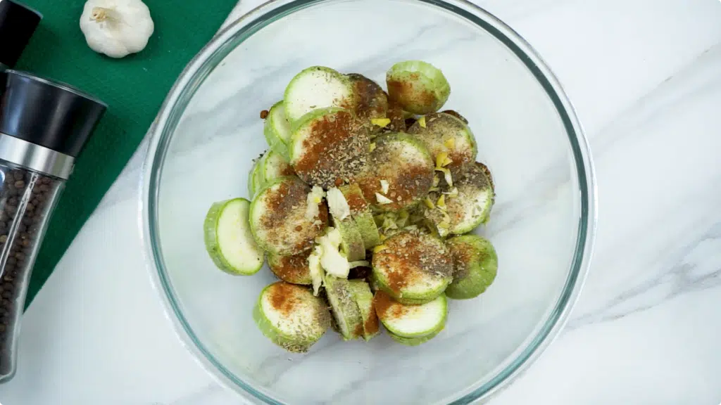 Sliced courgette in a glass bowl topped with spices