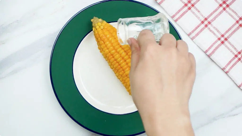 Pour a small pot of water over a single corn on the cob on a green-rimmed plate