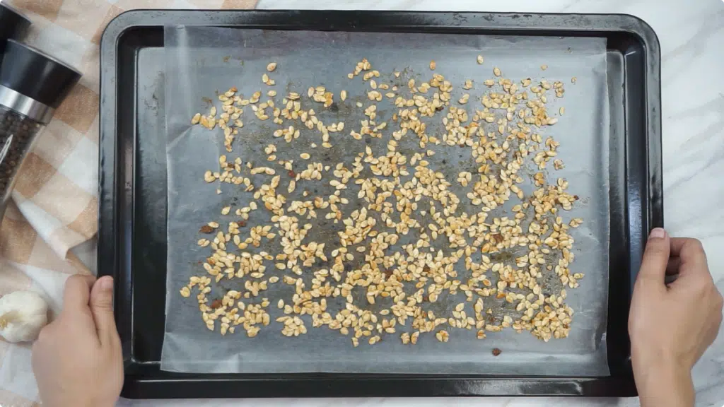 Raw melon seeds spread onto a lined baking tray