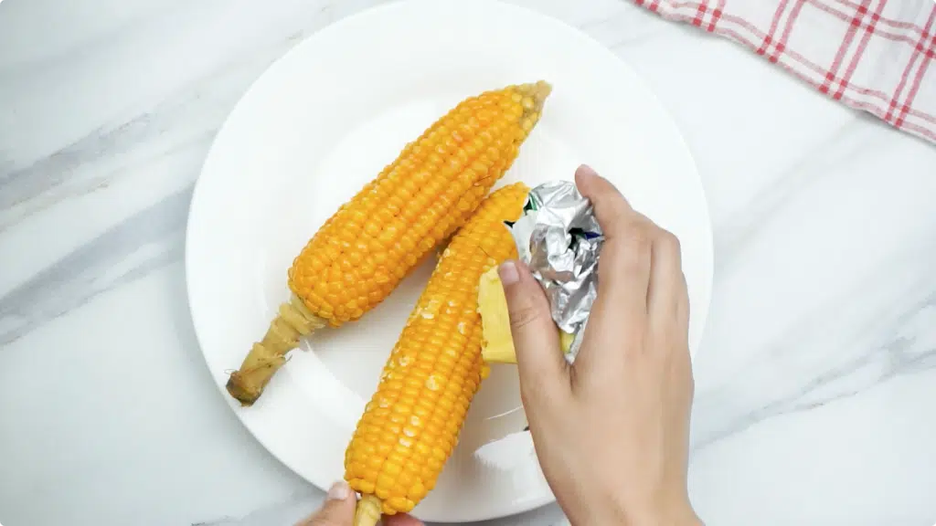 Rubbing cooked corn on the cob with butter wrapped in foil