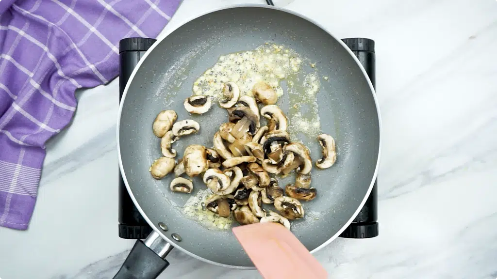Sauteeing steamed mushrooms in a pan with garlic