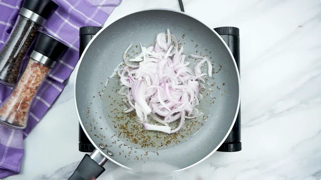 Toasted cumin in a pan with raw red onion slices