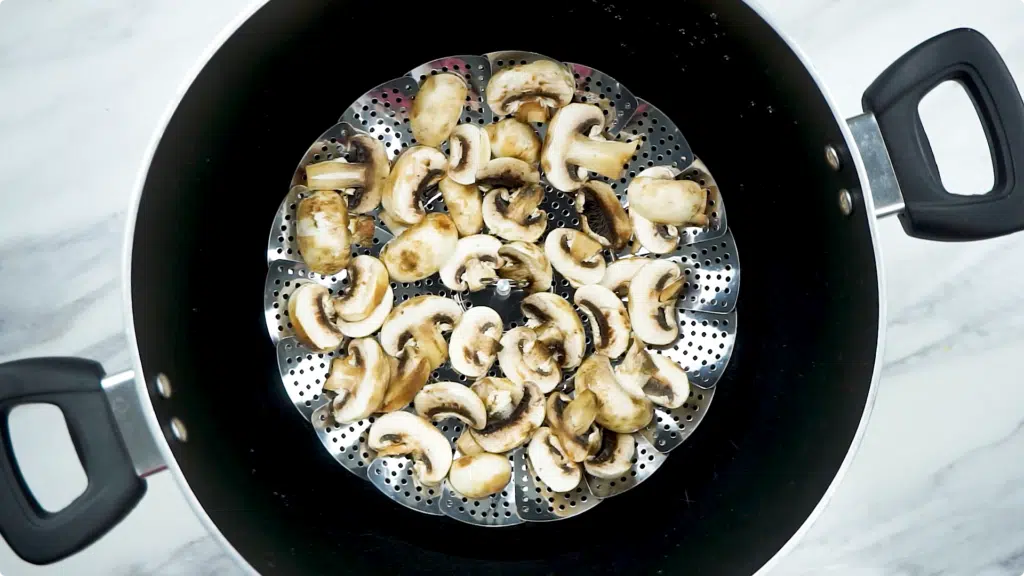 Steaming mushrooms in a large pan in a steamer basket