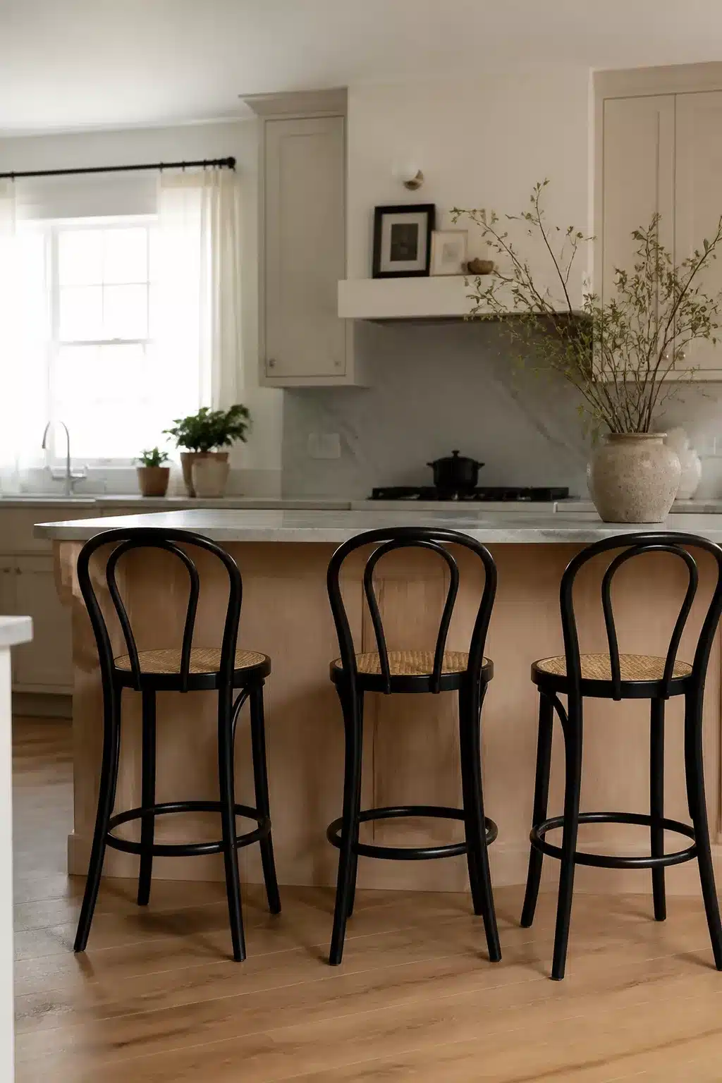 Three slim black bentwood kitchen bar stools with cane seats at a natural wood and marble island.