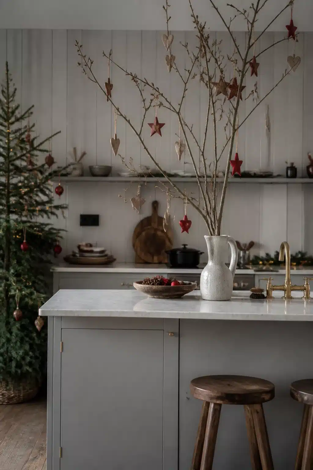 Scandi Christmas kitchen decor with bare branch ornament display, gray cabinets, marble island, and brass faucet