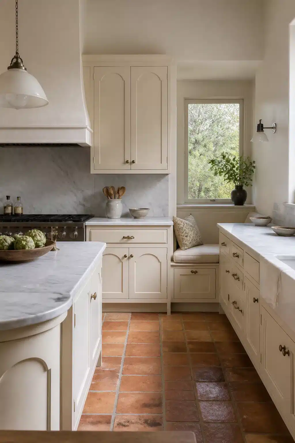 Cream kitchen cabinets with marble countertops, arched door details, and terracotta tile floor