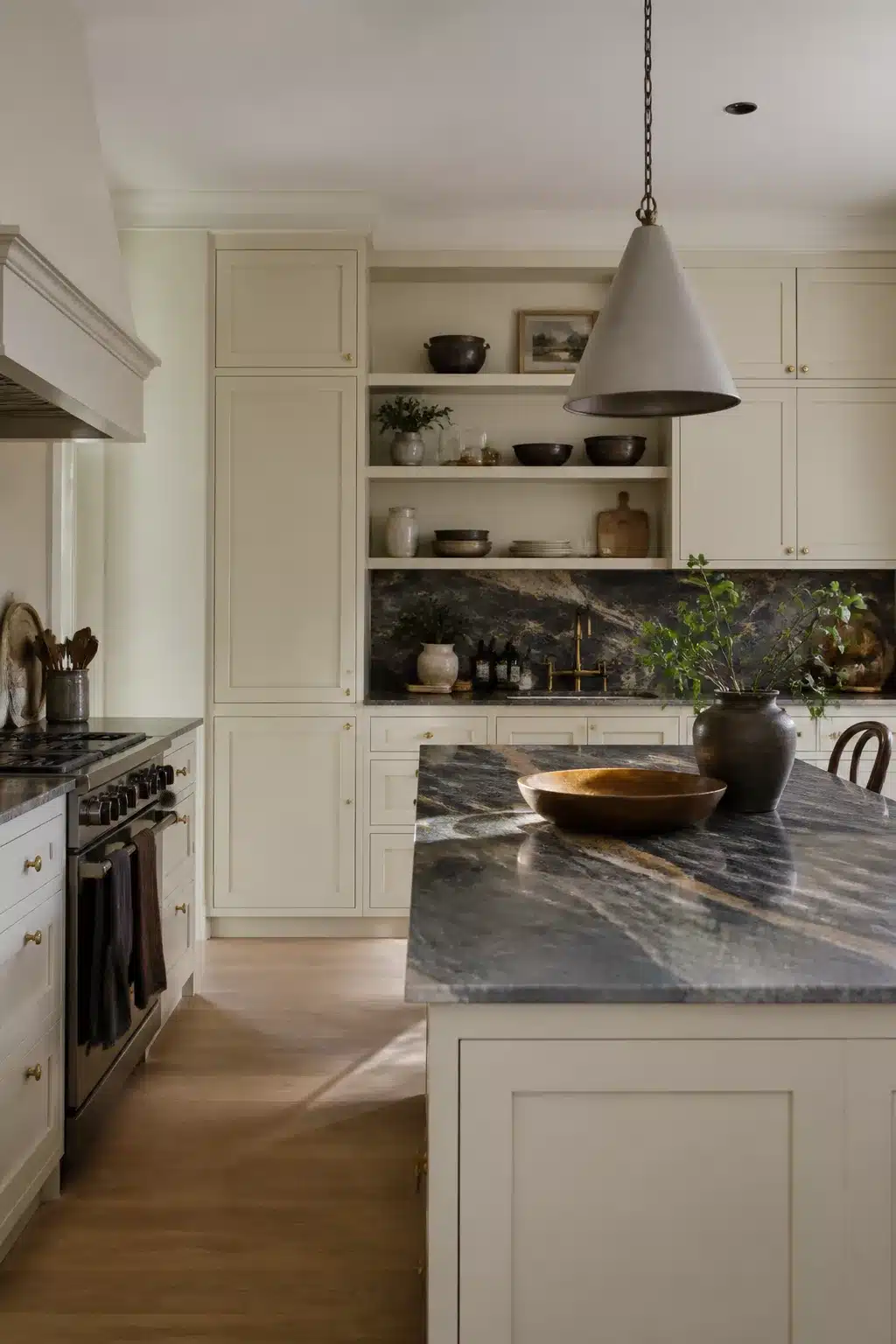 Cream kitchen cabinets with dark veined quartz countertops, slab backsplash, cone pendant, and brass hardware