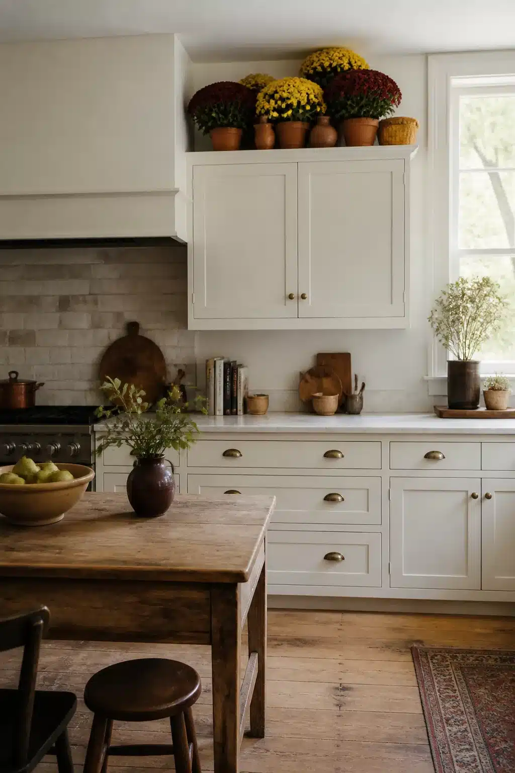 Fall kitchen cabinet decor with terracotta pots of burgundy and gold mums on top of cream shaker cabinets