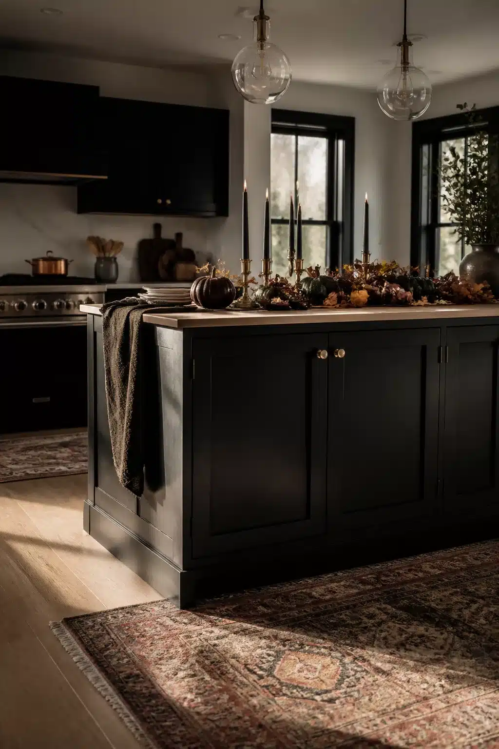 Fall kitchen island decor with black taper candles, brass candlesticks, and dark pumpkins on a butcher block island