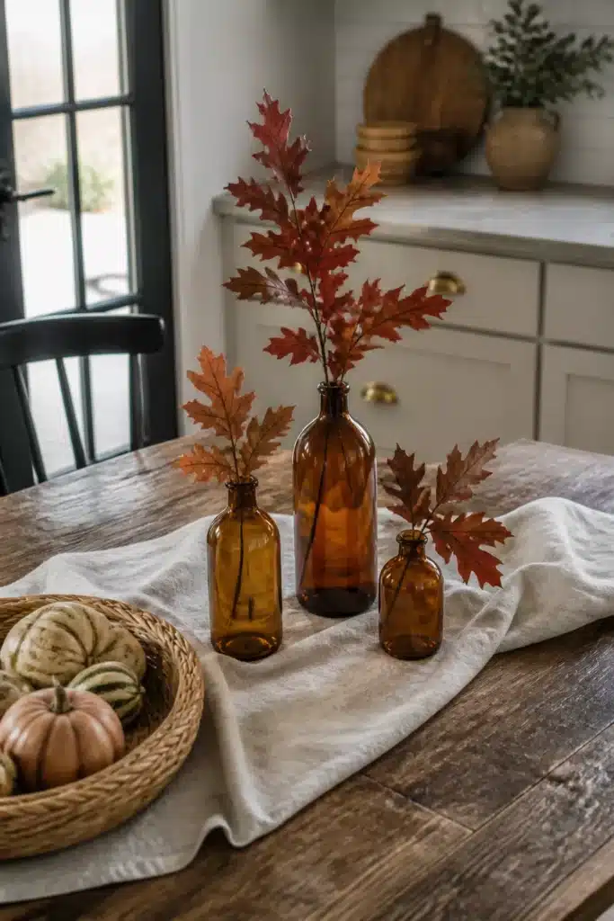 Fall kitchen table decor with amber glass bottles and rust oak leaf branches on a linen cloth