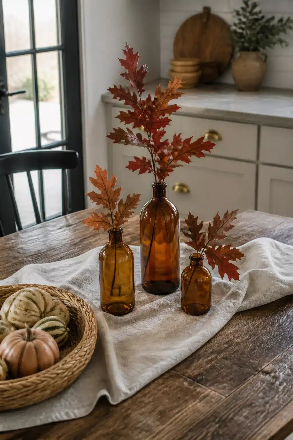 Fall kitchen table decor with amber glass bottles and rust oak leaf branches on a linen cloth