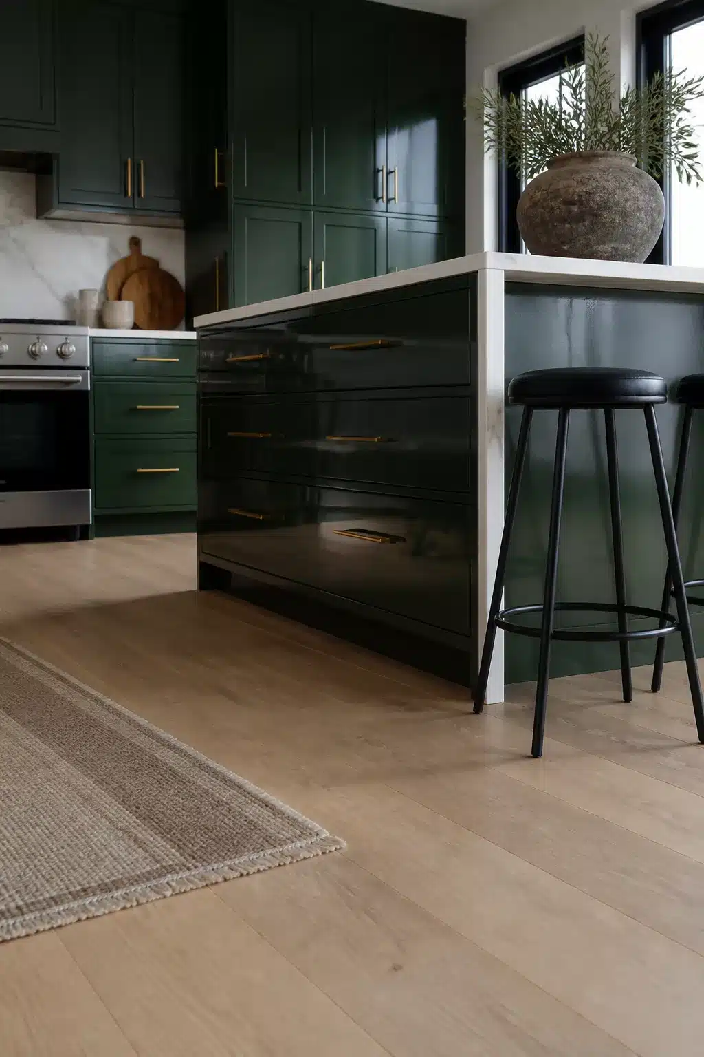 Racing green high-gloss kitchen island with gold tubular bar handles, matte green shaker cabinets, and light oak floors
