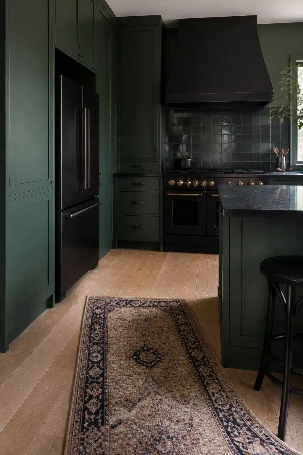 Forest green kitchen with black appliances, zellige tile backsplash, black range hood, and warm oak hardwood floors