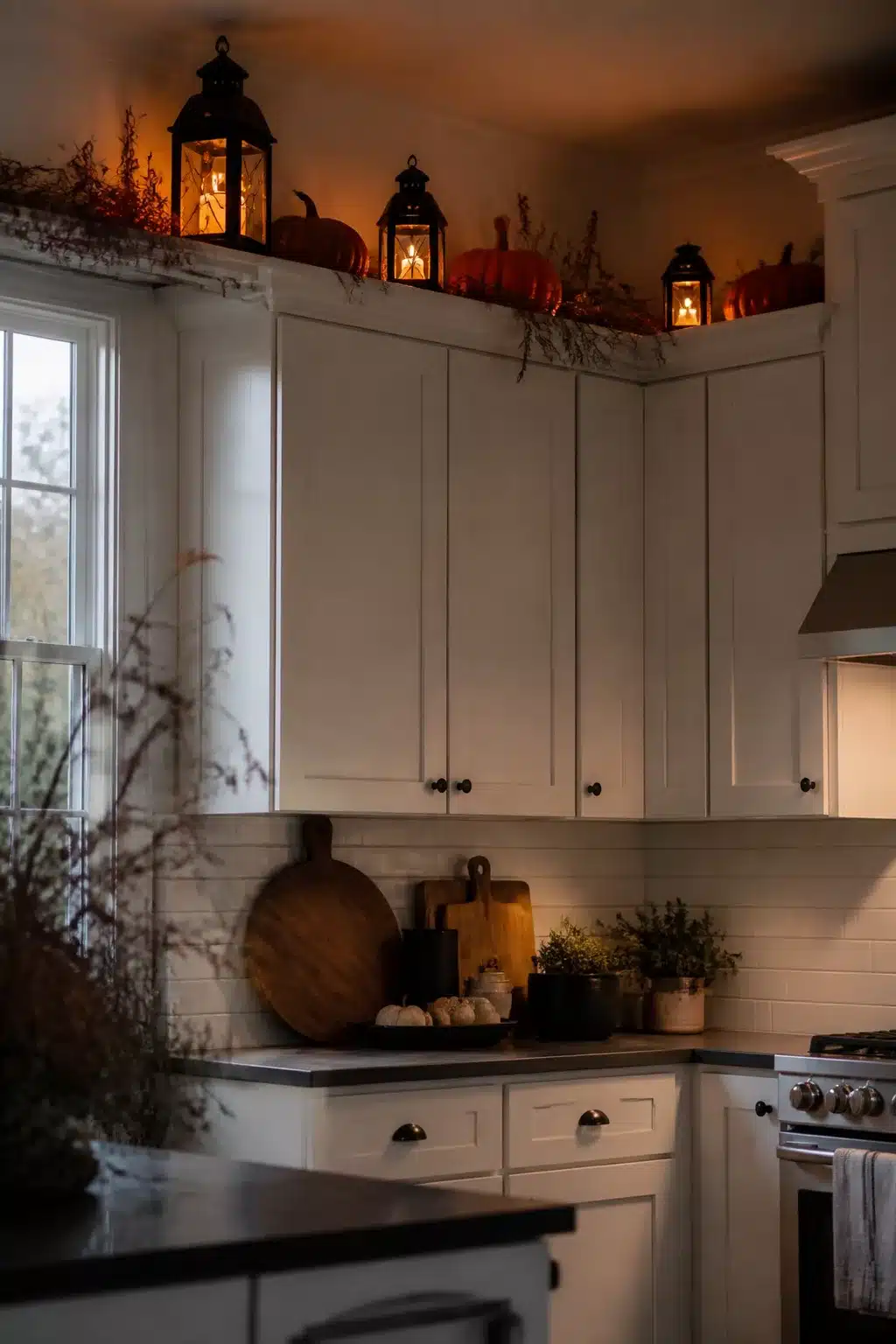 Halloween decor above kitchen cabinets — black lanterns glowing with orange pumpkins on white shaker cabinets