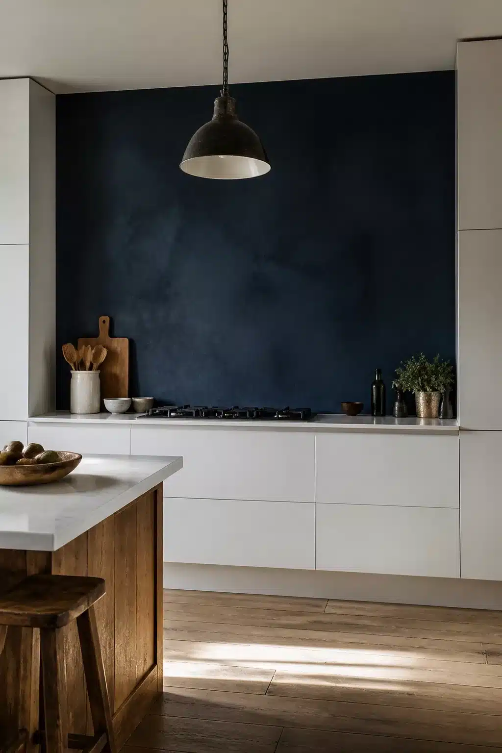 Navy kitchen accent wall with concrete-effect finish, white flat-front cabinets, marble countertop, and iron pendant light.