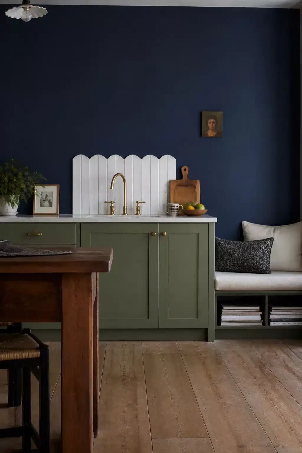 Navy kitchen accent wall with sage green shaker cabinets, scallop tile backsplash, and brass faucet