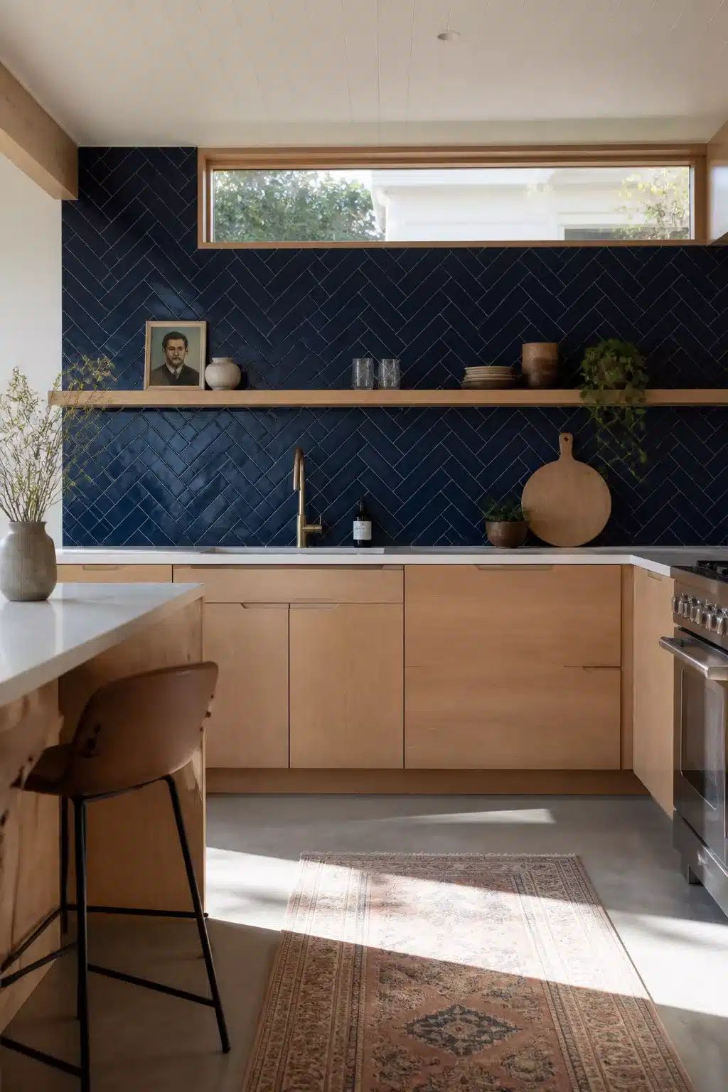 Navy kitchen backsplash in a herringbone pattern with warm oak cabinets, brass faucet, and open wood shelving.