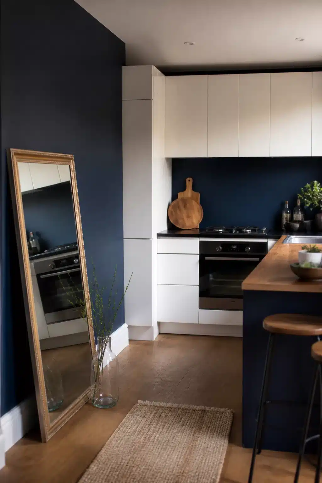 Small kitchen with navy blue walls, white flat-front cabinets, and a leaning gold-framed floor mirror