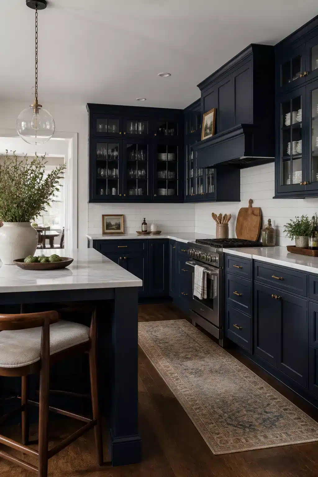 Navy kitchen with marble countertops featuring glass-front upper cabinets, brass hardware, and a stainless range