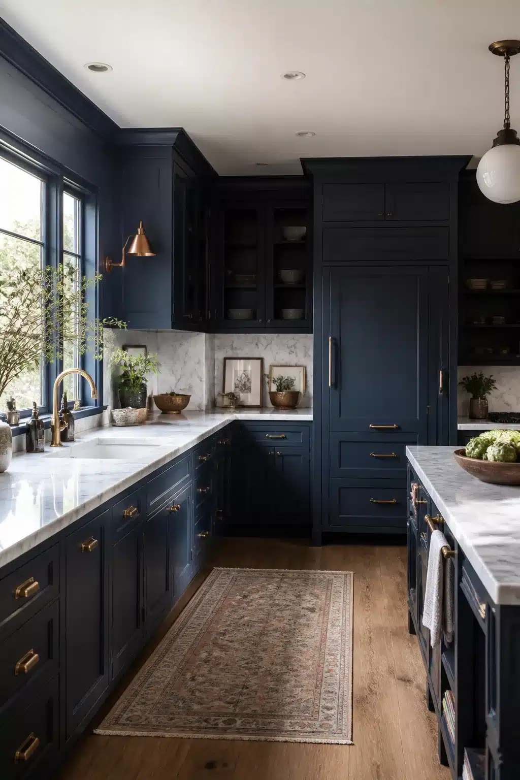 Navy kitchen with marble countertops featuring a fully paneled refrigerator flush with dark blue cabinetry and brass hardware