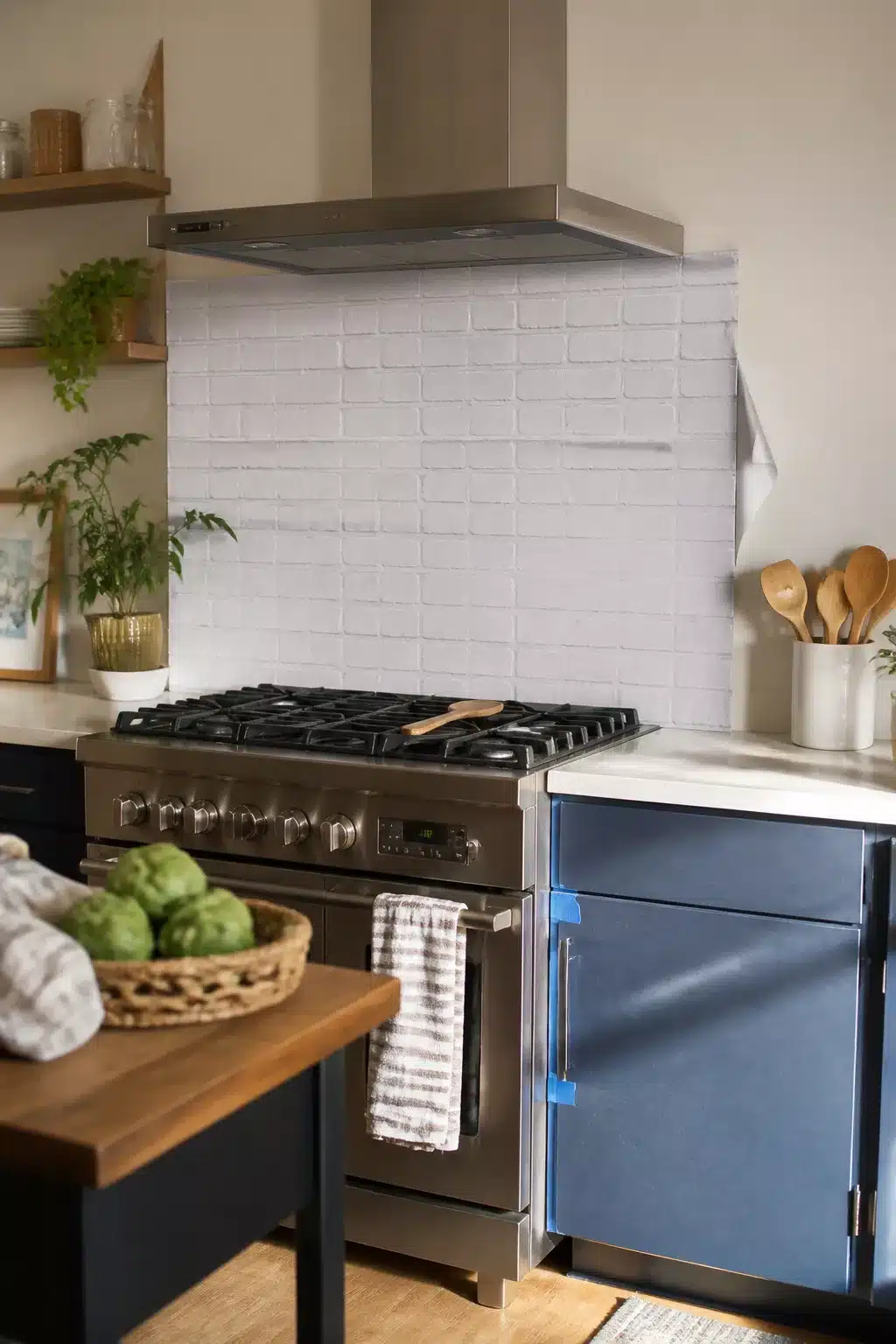Temporary rental kitchen makeover with stick-on white brick wallpaper behind a stainless range and blue cabinets.