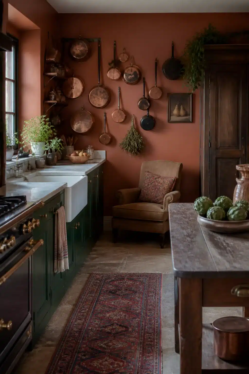 Terracotta kitchen walls with forest green cabinets, copper pans displayed on wall, farmhouse sink, and Persian rug