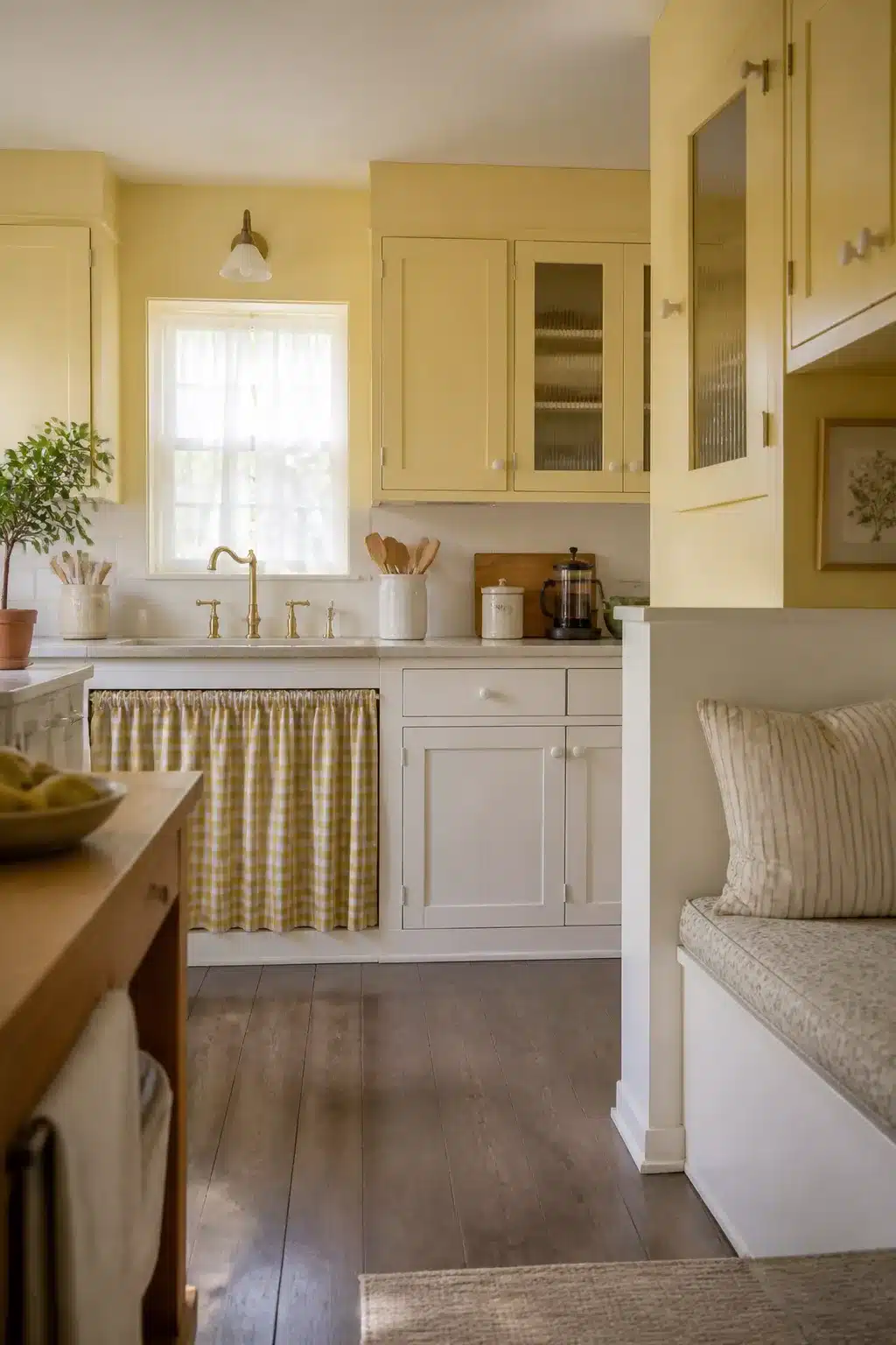 Two tone kitchen cabinet ideas with pale yellow upper cabinets and soft white lowers with brass faucet and gingham sink skirt.