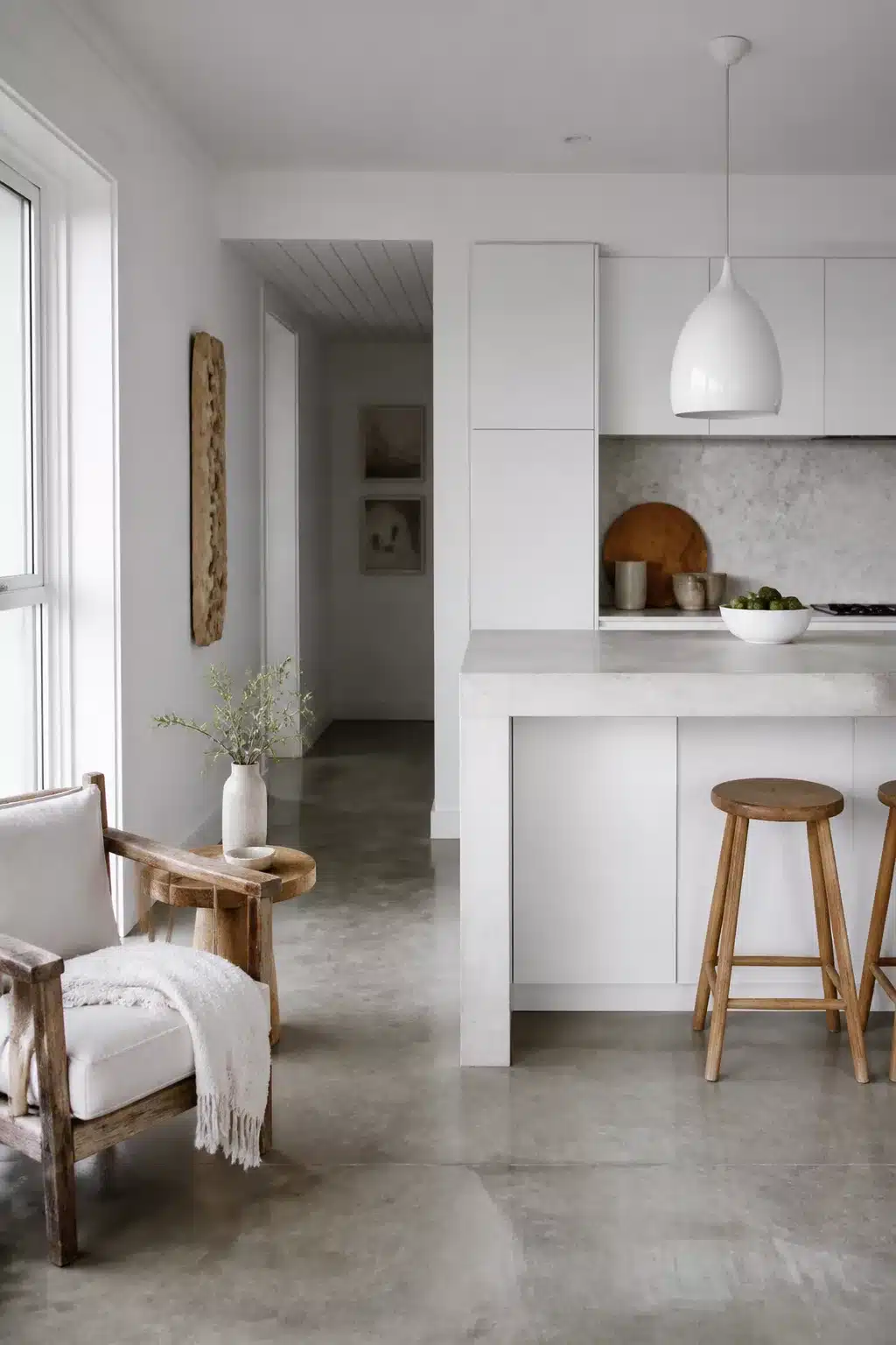 White coastal kitchen with poured concrete island, polished concrete floors, and timber barstools