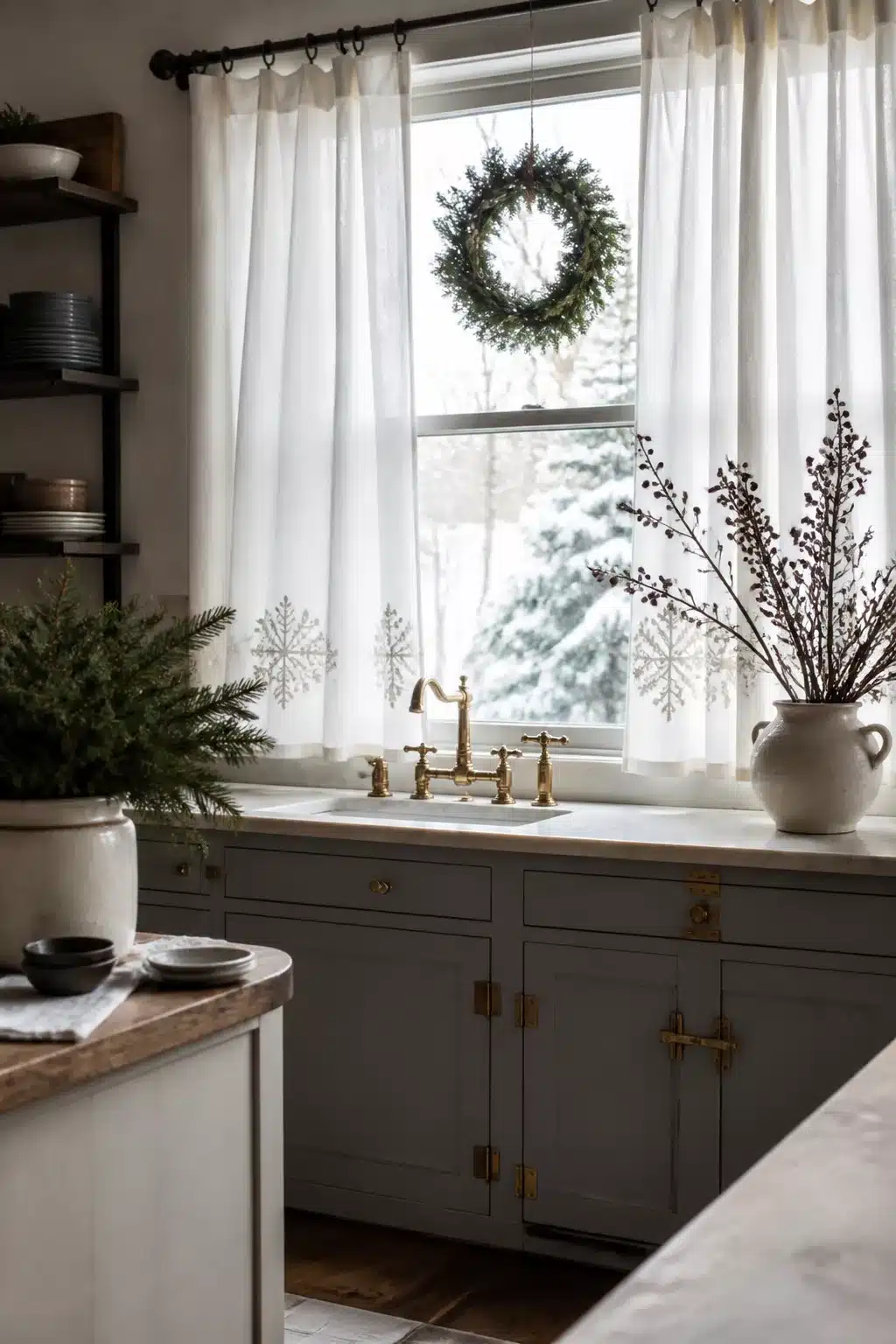 Winter kitchen decor ideas with sheer snowflake linen curtains, gray cabinets, brass hardware, and a wreath over the sink window.