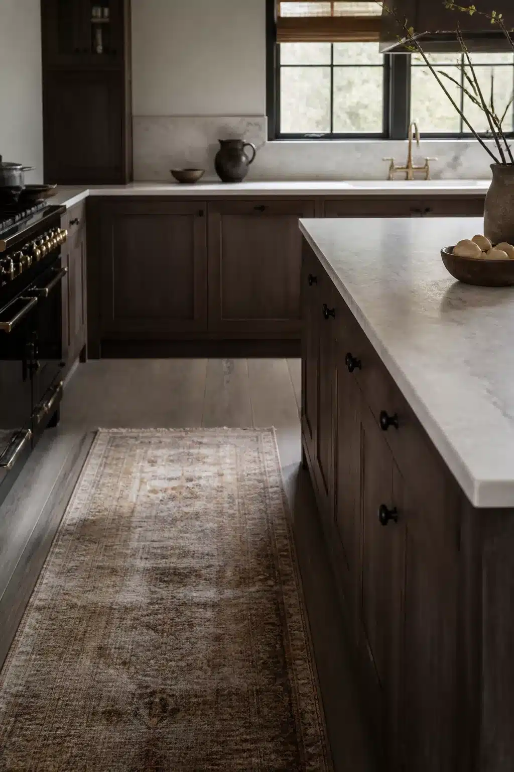 Fumed oak wood kitchen cabinets with honed white marble countertops, black hardware, and a vintage runner rug