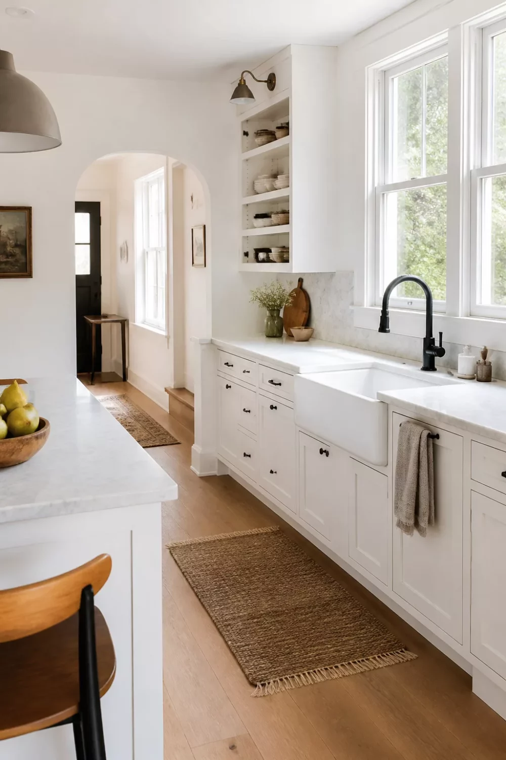 Matte black kitchen faucet over a white apron-front farmhouse sink in a bright white shaker kitchen