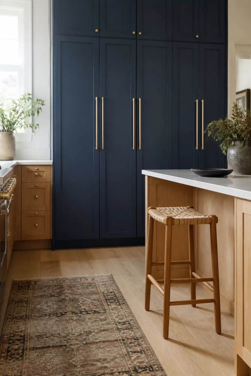 Blue kitchen cabinets with gold hardware — midnight navy pantry wall, brass bar pulls, and warm oak island