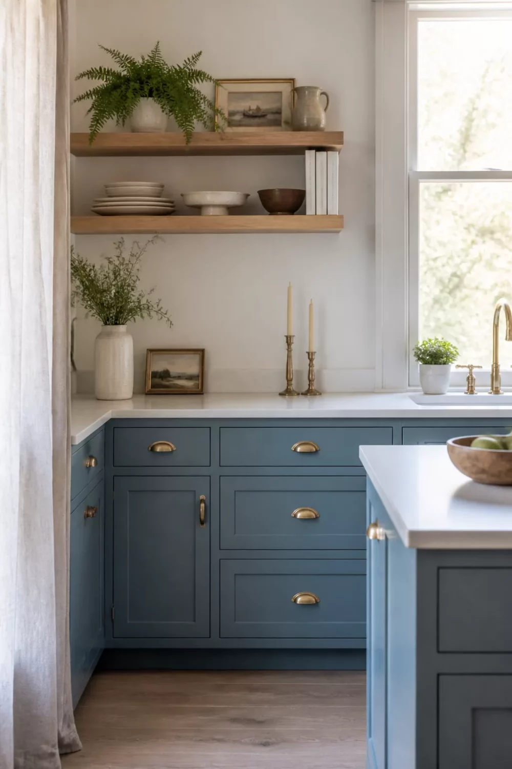 Muted blue kitchen cabinets with gold cup pulls, white quartz counters, and warm oak floating shelves.
