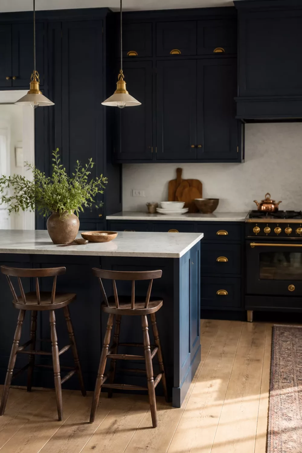 Inky navy blue kitchen cabinets with gold brass cup pull hardware, marble countertop, and brass pendant lights