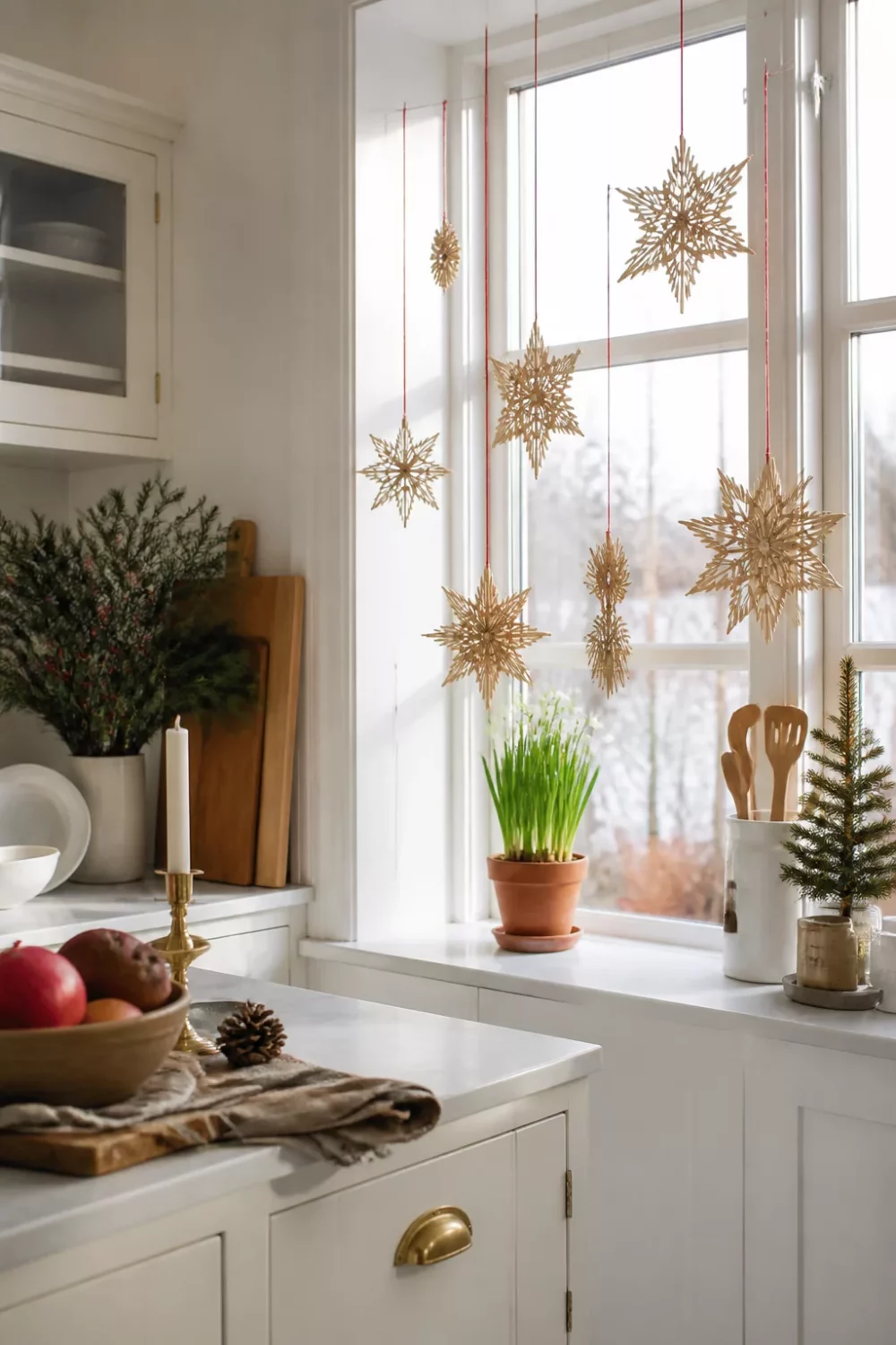 Gold straw star ornaments hanging in a white kitchen window — Scandinavian Christmas kitchen ideas with Nordic festive decor.