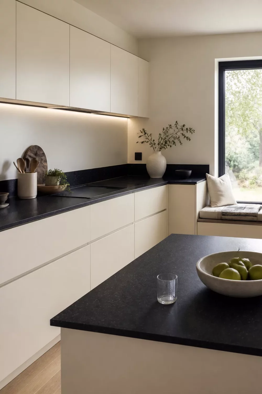 Cream kitchen with black countertops, handleless flat-front cabinets and warm LED under-cabinet lighting