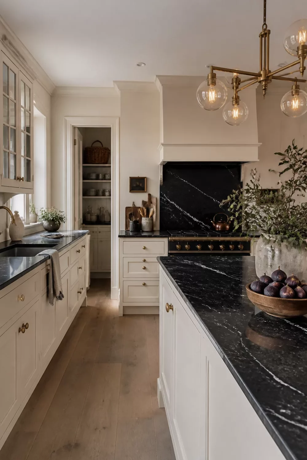 Cream kitchen with black countertops featuring Nero Marquina marble backsplash, brass hardware, and globe pendant lights