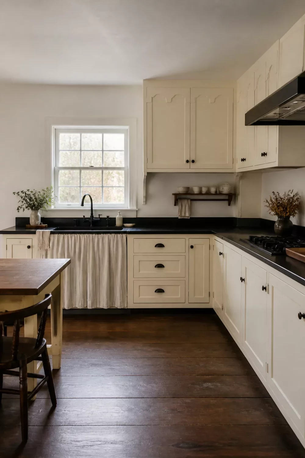 Cream kitchen with black countertops featuring scallop detail cabinet doors, linen sink skirt, and dark wood floors