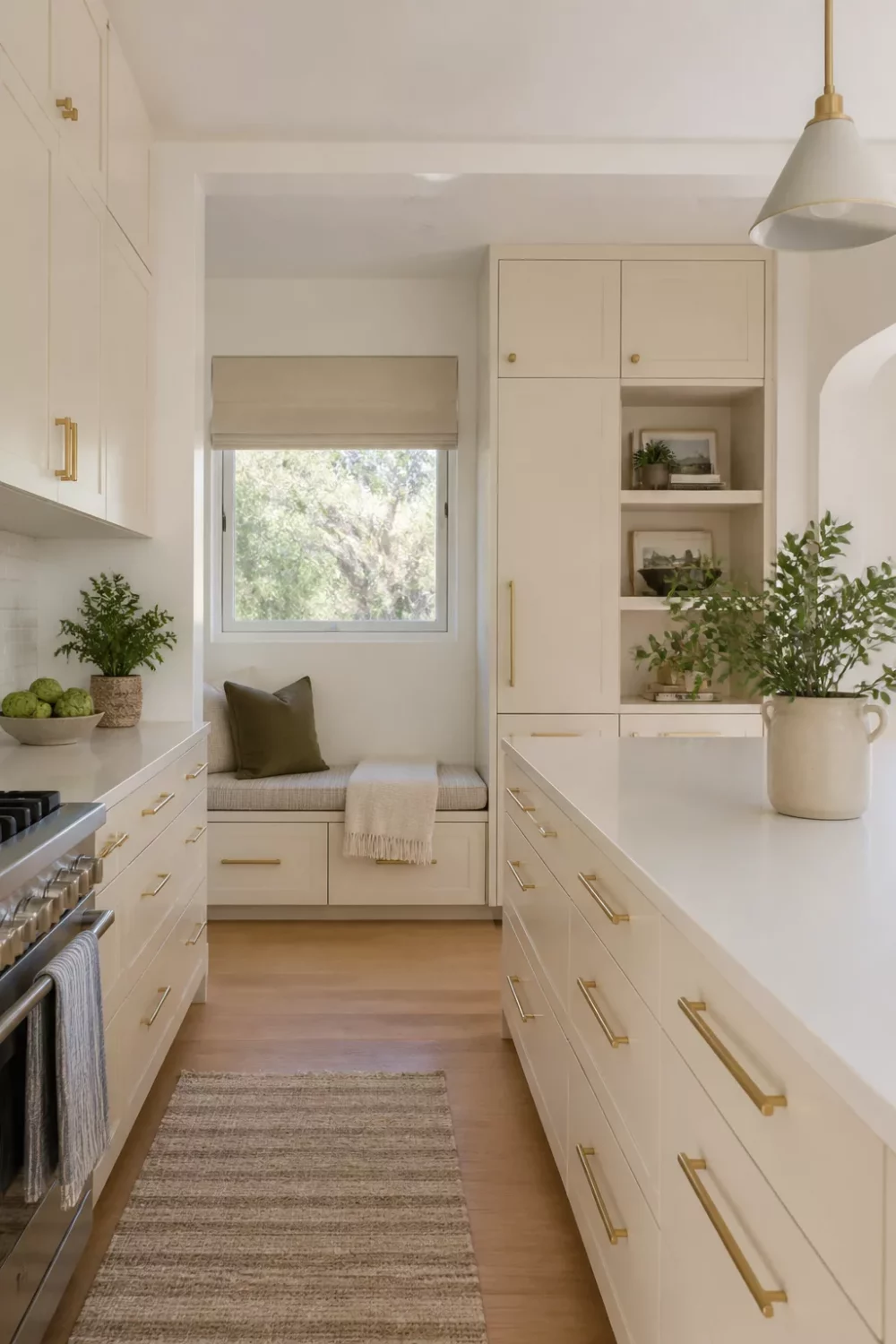 Cream kitchen with brass handles, built-in window bench, sage pendant light, and warm oak floors