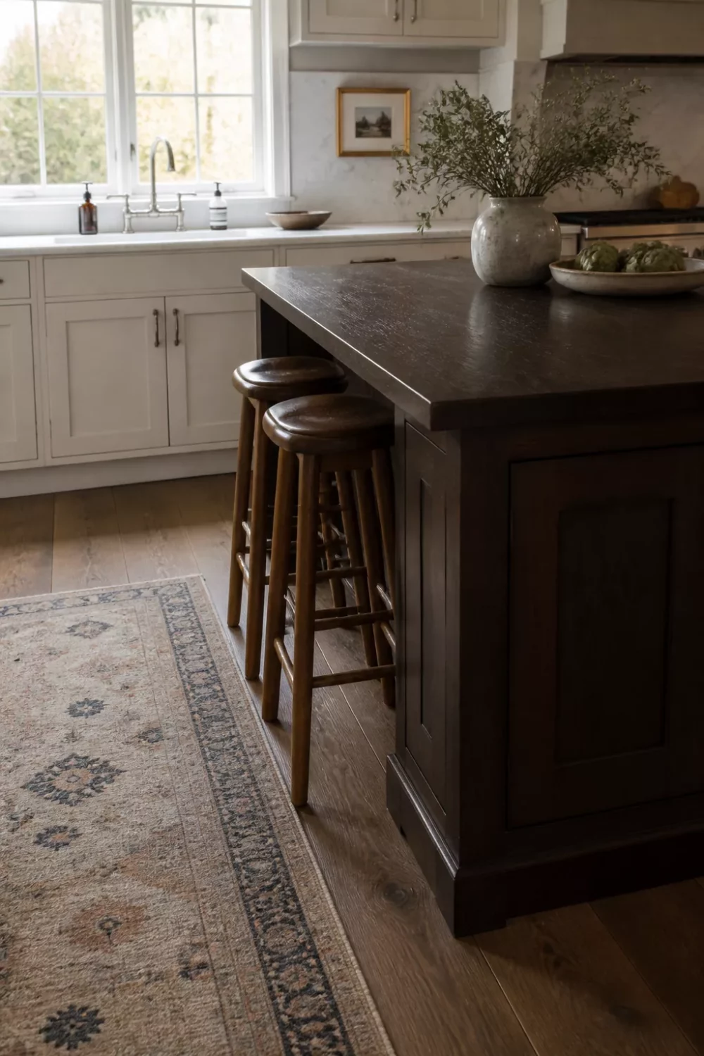 Dark wood kitchen countertop on a navy island beside white marble perimeter cabinets with spindle stools