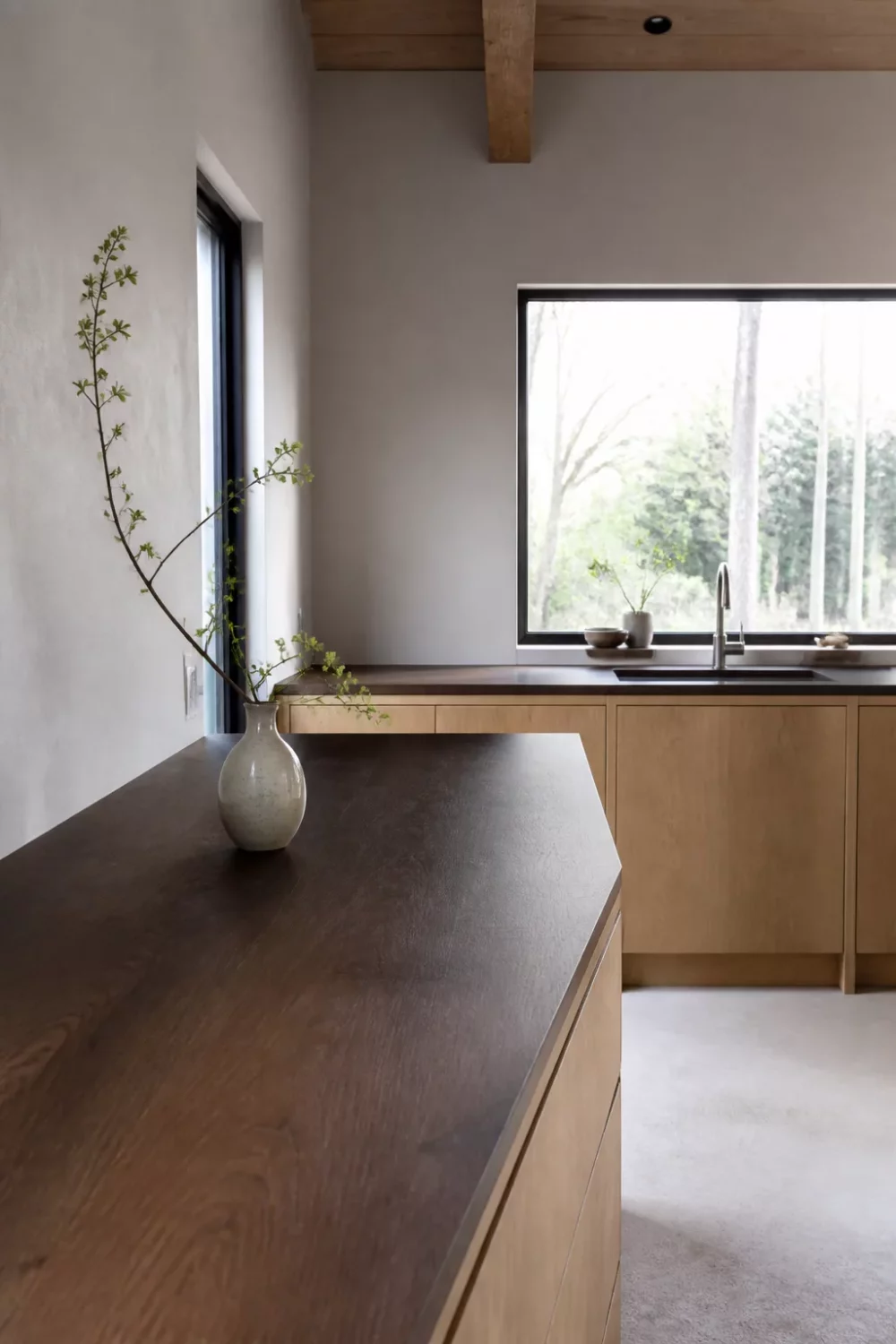 Dark wood kitchen countertop on pale oak cabinets in a minimal Japandi kitchen with plaster walls and timber beams