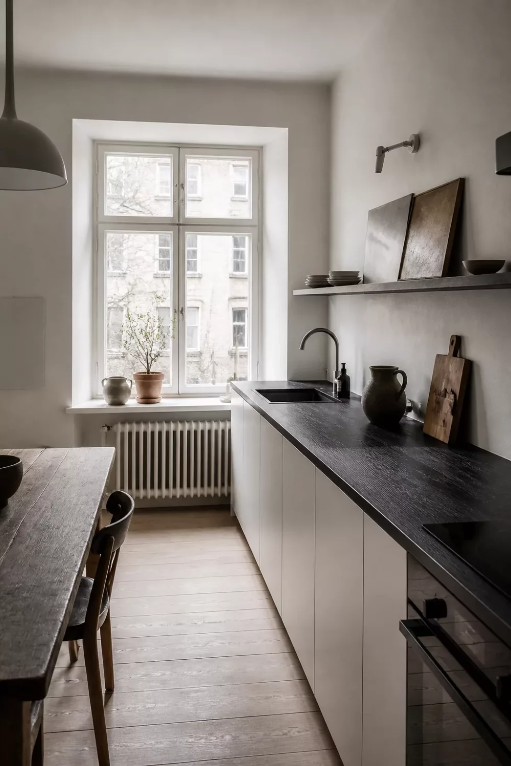 Ebonized oak dark wood kitchen countertop with white handle-free cabinets and floating shelf in minimalist kitchen