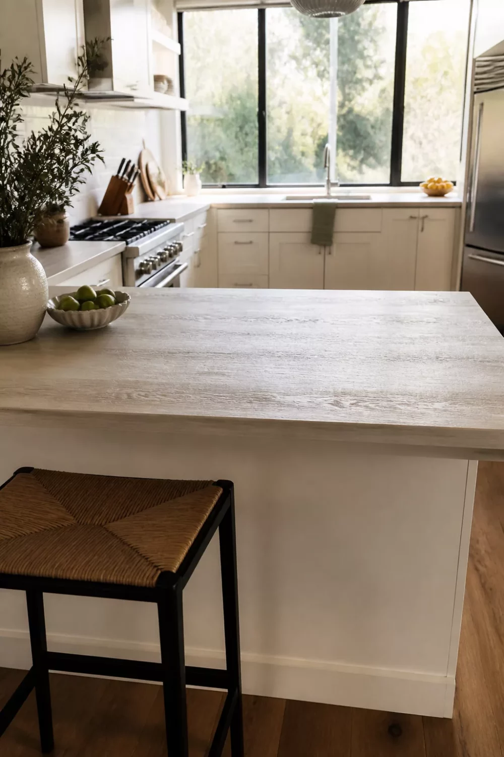 Whitewashed faux wood kitchen countertop on a bright island with rush seat stools and cream cabinets